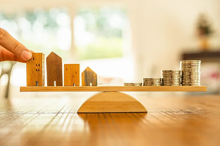 Holzhaus und Münzen stapeln sich mit Waagschale. Geldmanagement, Finanzplan, Zeitwert des Geldes. Immobilien- und Immobilienmakler bieten Hauskonzepte an.