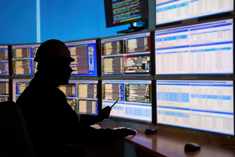 SCADA-System im Zentralheizungsprozess. Silhouette eines Bedieners, der Daten auf mehreren Monitoren auswertet - für optimale Leistung und Sicherheit in industriellen Automatisierungssystemen.