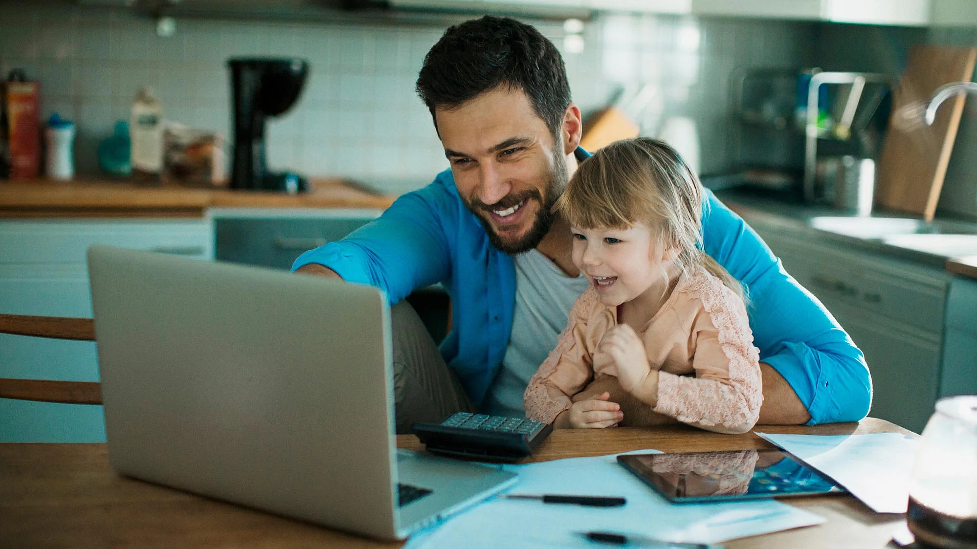 Lächelnder junger Mann, der mit kleiner Tochter auf dem Schreibtisch auf den Laptop schauend