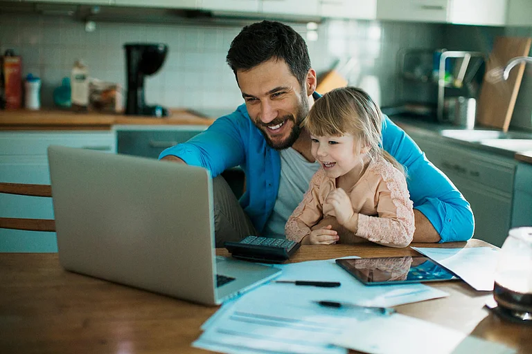 Lächelnder junger Mann, der mit kleiner Tochter auf dem Schreibtisch auf den Laptop schauend